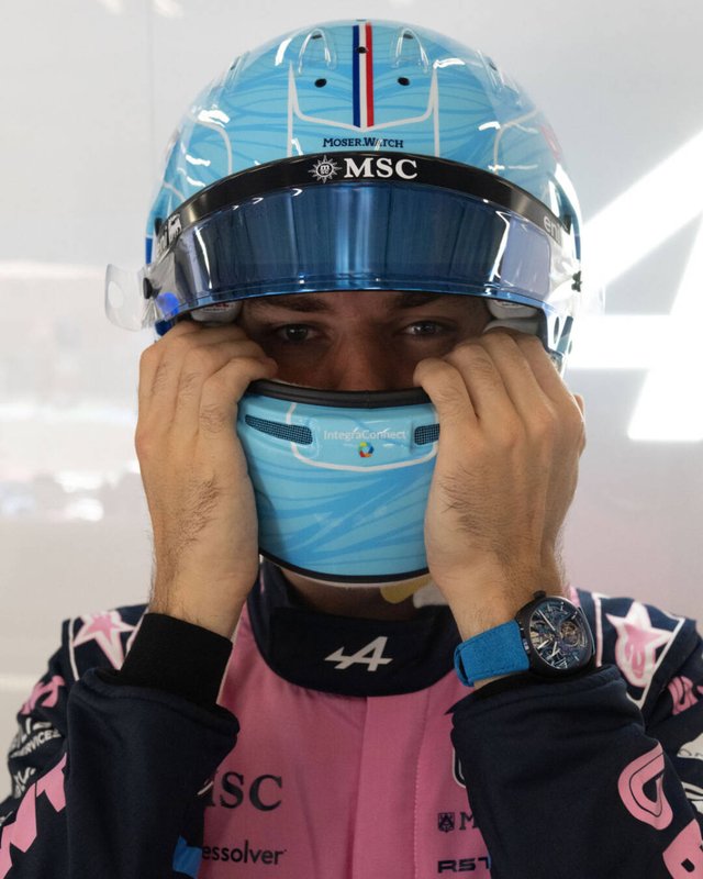 A driver in a blue helmet adjusting the visor, watch on the wrist
