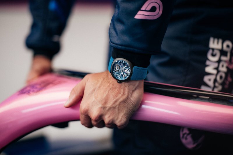 A hand on a pink steering element, wearing the watch
