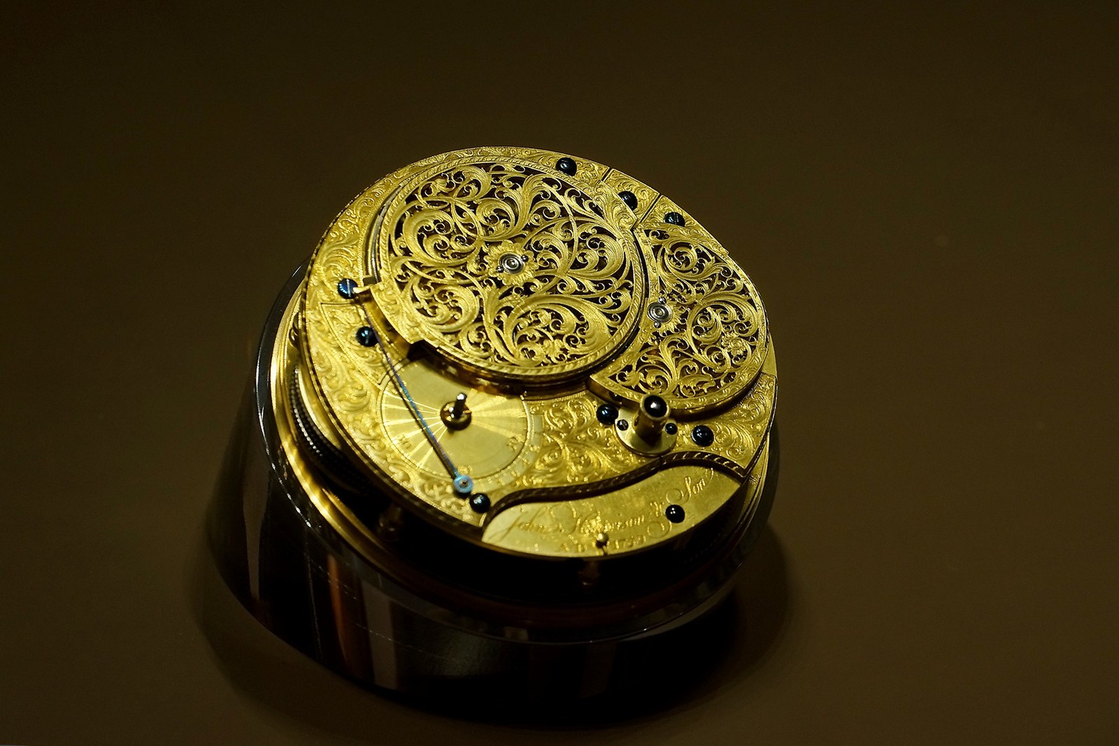 The ornately pierced and engraved gilt movement of Harrison's H4, displayed under glass on a dark stand